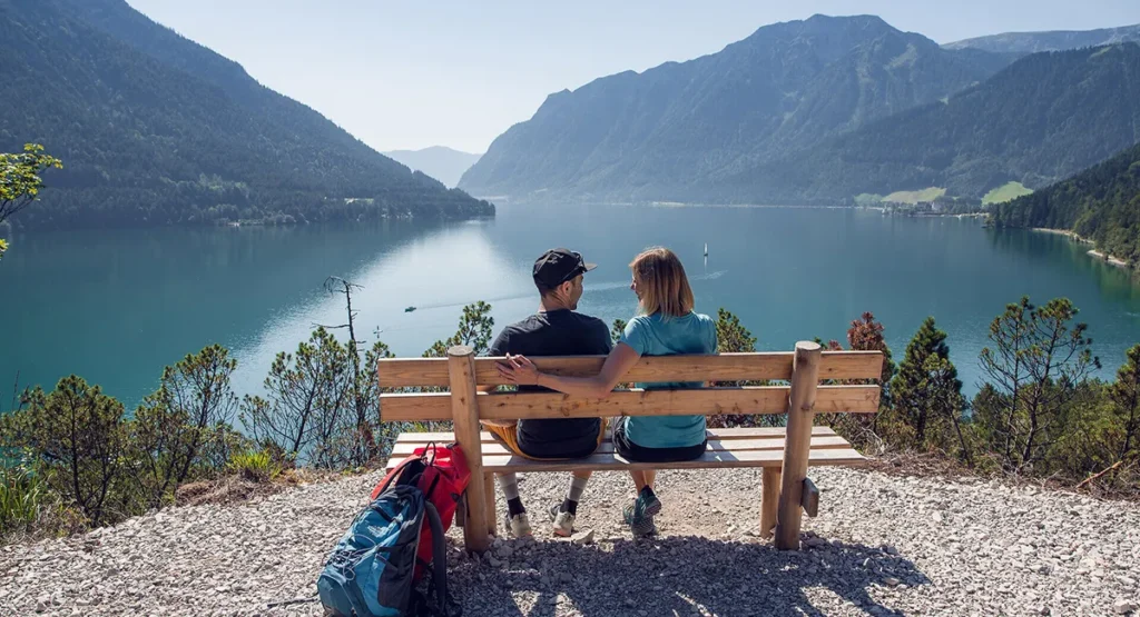 Ein Paar sitzt auf einer Bank, wandern am Achensee, mit Blick auf einen Bergsee und Hügel.