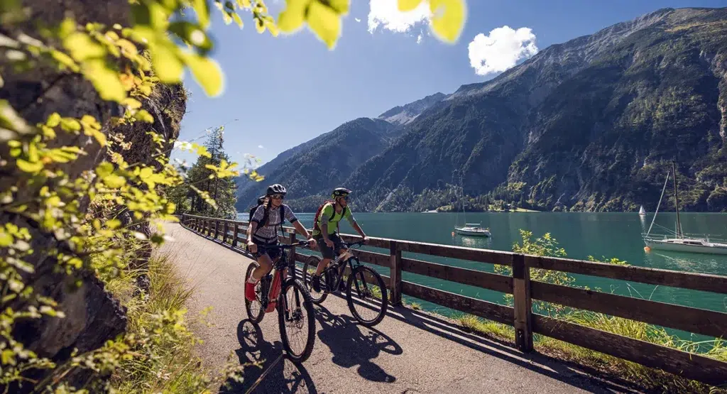 Zwei Personen beim Radfahren neben berg und see am Achensee, mit Blick auf Berge und Boote.